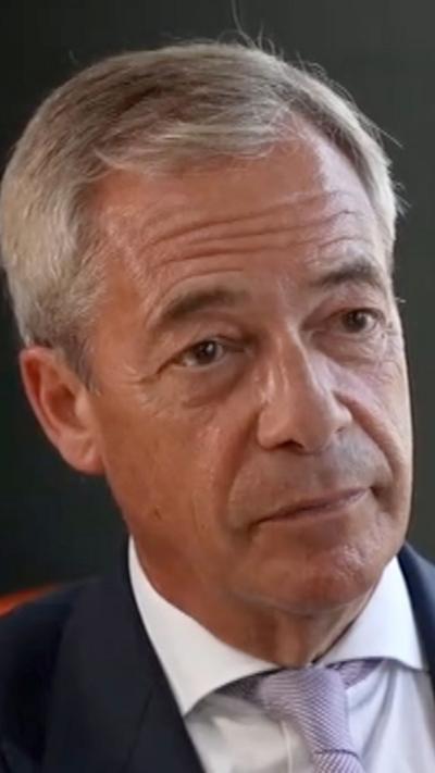 Nigel Farage's face. He is wearing a white shirt, lilac tie and dark jacket.