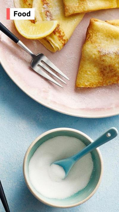 A plate of flat pancakes with lemon and white sugar