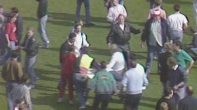 Sarah Hicks being carried from the pitch by spectators on a makeshift stretcher