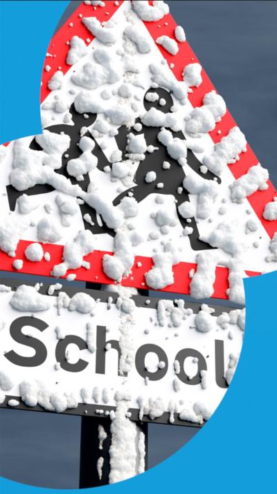 A school road sign on a pole covered in snow with a dark grey cloudy sky behind
