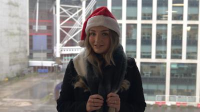 Charlie Buckland wearing a santa hat and a scarf. she has long blond hair and is wearing a coat.