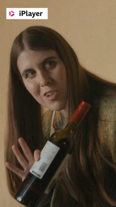 A woman with long brown hair holds an opened bottle of red wine in one hand