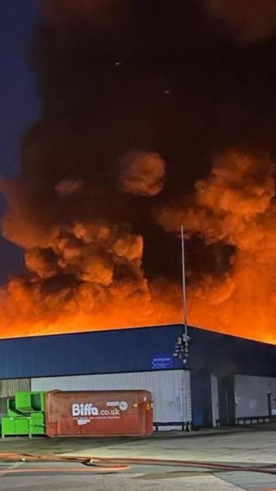 Flames light up a rising cloud of black smoke above a warehouse