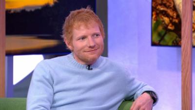 Ed Sheeran wearing a blue jumper while sitting on the One Show sofa. He's looking to the right and giving a small smile