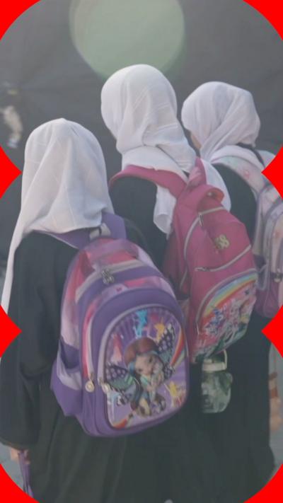 Three young girls wearing head coverings and pink and purple backpacks with cartoon characters on them,