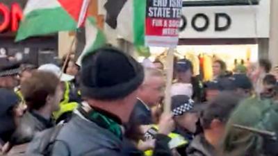 Michael Gove surrounded by police and protesters waving Palestinian flags