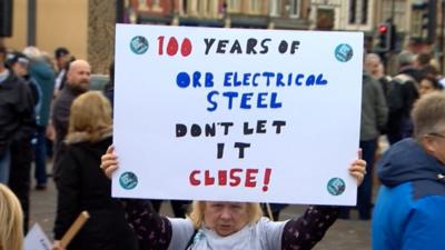 A woman holding up a sign against steel closure