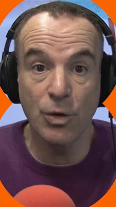 A man, Martin Lewis wears a purple jumper and headphones and looks at the camera