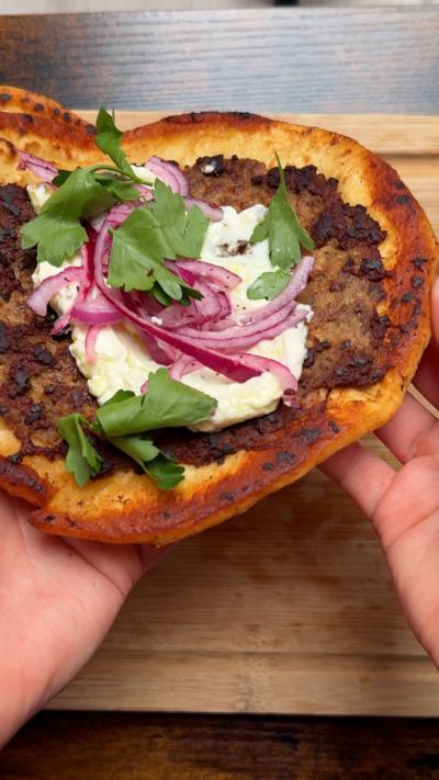 Smashed lamb flatbread on a wooden chopping board being lifted up 