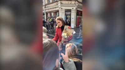 Princess of Wales pictured greeting crowds holding flowers in a red coat 