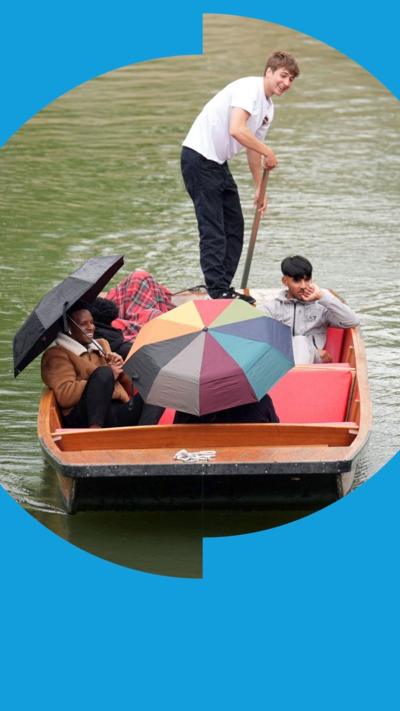 Passengers in a punt hold up umbrellas as they travel along the River Cam 