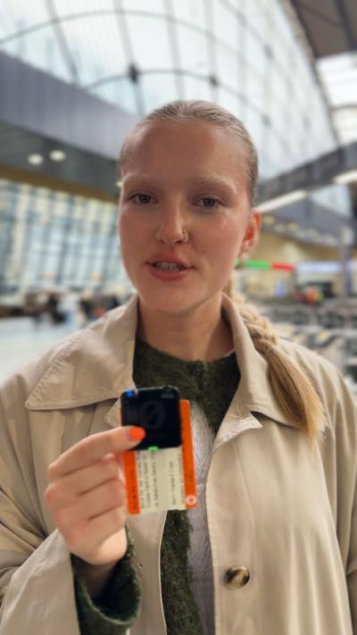 Woman standing in a train station holds small microphone and train ticket.