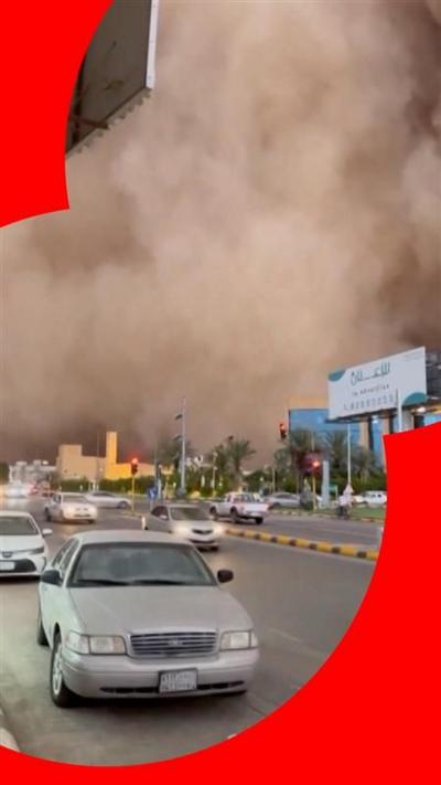 Cars drive down road as huge sandstorm cloud looms in the background 
