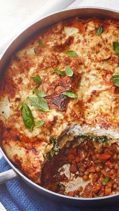 A round pan of lasagne. One portion has been taken out, with lentils on the bottom of the pan and crispy cheese on the top.