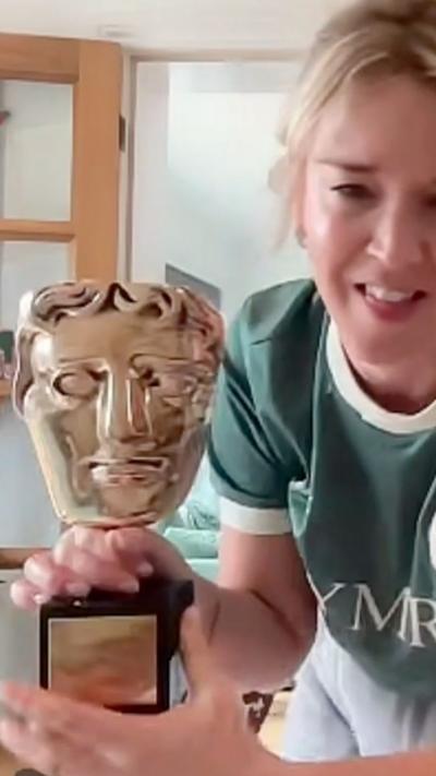 A blonde woman in a green shirt that says Cymru holding a gold Bafta trophy