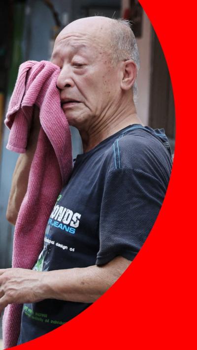 An older man holds a towel to his face to dry his sweat standing outside