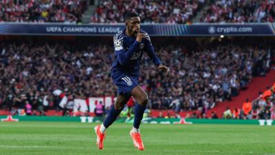 Ousmane Dembélé is playing on the pitch wearing the dark navy Paris Saint-Germain F.C kit.