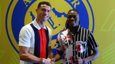 Clara Luvanga gives a thumbs up and shakes hands with Cristiano Ronaldo in front of a yellow and blue Al-Nassr logo