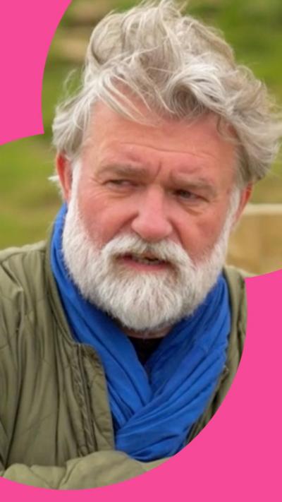 Hairy Biker Si King standing in a field, looking angry and upset. He has short grey hair and a beard, and is crossing his arms