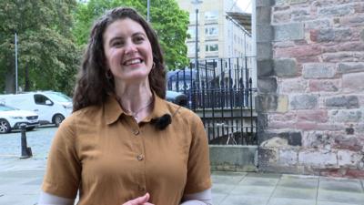 Màiri Britton, Oifigear Gàidhlig ùr Oilthigh Dhùn Èideann, na seasamh taobh a-muigh na toglaich