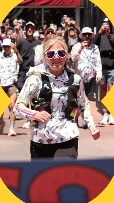 Rachel Entrekin approaches the finish line at the Cocodona 250 ultramarathon. She is wearing a white jacket and white sunglasses.