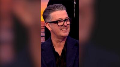 David McCormack, the voice of Bandit Heeler, smiles. He wears black glasses and has swept back grey hair.