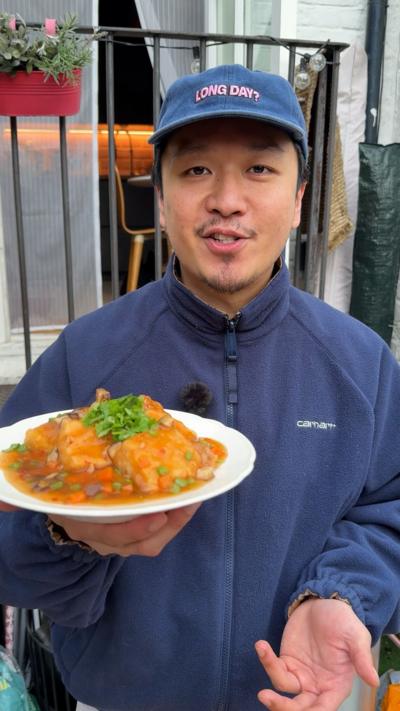 A man in a blue jacket and baseball cap holds up a plate of food.