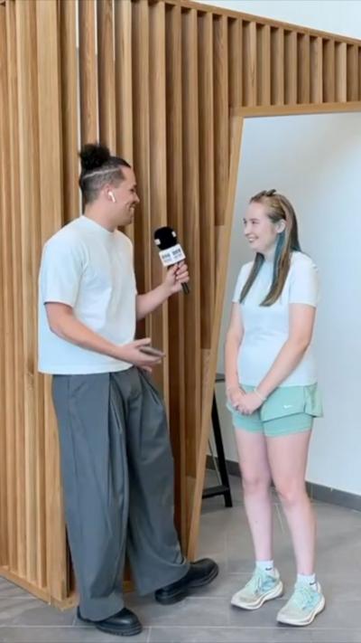 A BBC reporter with a bun chatting to a student in a white T shirt and turquoise shorts