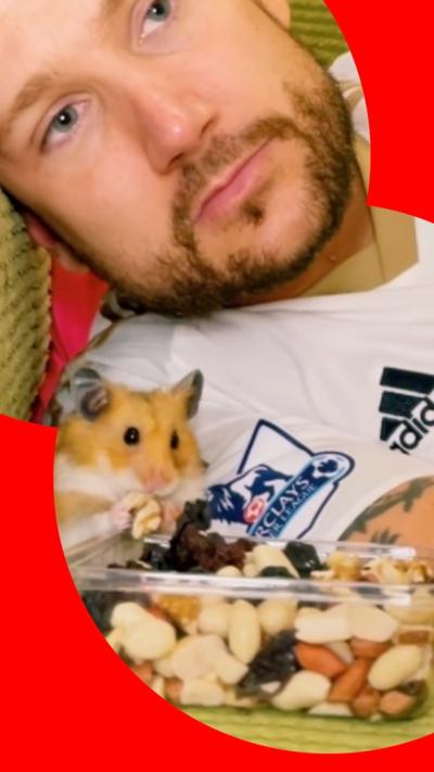 Man on sofa with a little hamster who is snacking on nuts 