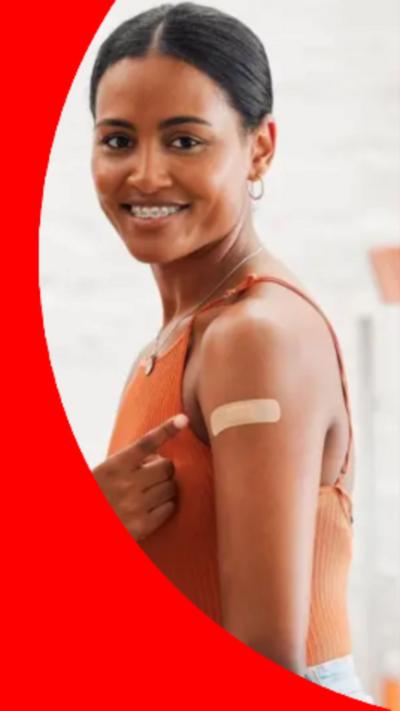 A woman with dark hair pulled back from her face points to a plaster on her arm 