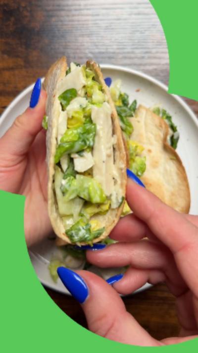 Chicken Caesar tacos on a white plate with one being lifted up so you can see the filling 