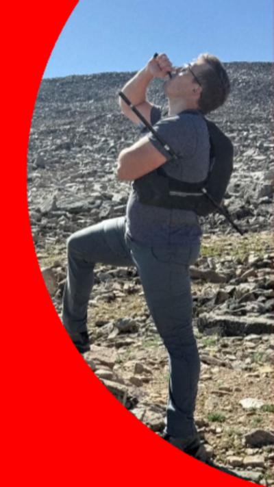 Hiker drinking from a bottle with a hiking pole piercing his torso on a rocky mountain trail