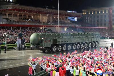 Military parade in Pyongyang with a huge missile and crowds of brightly clothed supporters waving flags