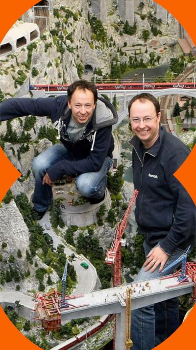 Frederik and Gerrit Braun pose in front of a model mountain terrain with a train track