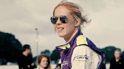 Image of a woman in racing overalls with aviator sunglasses