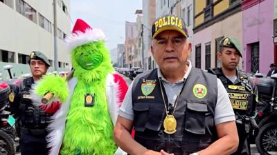 A police officer dressed as the Grinch standing next to police