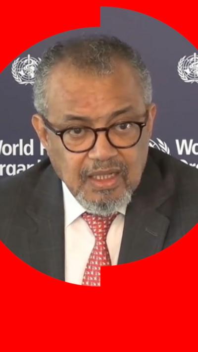 Dr Tedros, who has greying hair and dark-rimmed glasses, sits in front of a board displaying the WHO logo