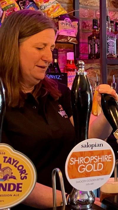 Woman with long brown hair and a black top pulling a pint behind a pub bar