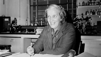 Dorothy Hodgkin sits at a desk, writing