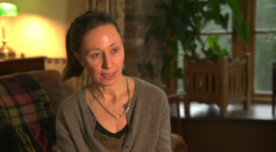 Dr Bernadette Hard, in a brown cardigan, talking about her experience of a rare brain/spinal condition while abroad