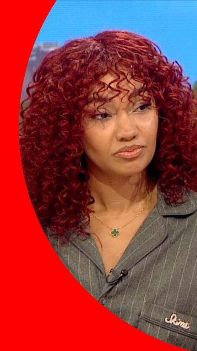 Leigh-Anne Pinnock has curly red hair and wears a grey pinstriped shirt