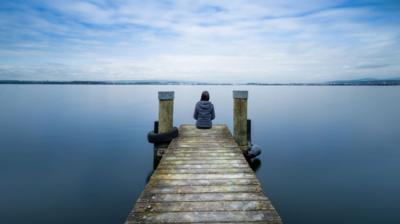 A person sits on the end of a pontoon looking out over a tranquil lake