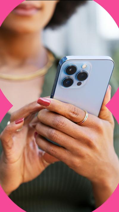 A woman wearing a green top is holding a light blue mobile phone in her hand and using her other hand to press on the screen.
