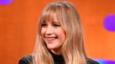 Jennifer Lawrence smiles in the Graham Norton Show studio. She has long brown hair and wears a black top