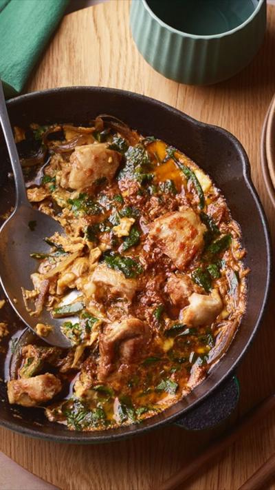Top down view of a brown dish with chicken in a sauce with a spoon in it