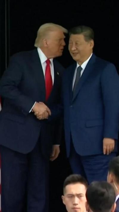 Donald Trump speaking into Xi Jinping's ear as they shake hands