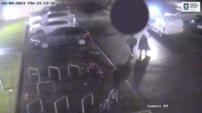 CCTV of a dark leisure centre car park, two people walking, with a black circle over the victim