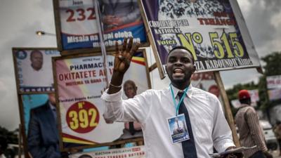 Man next to billboards with candidates in Kinshasa