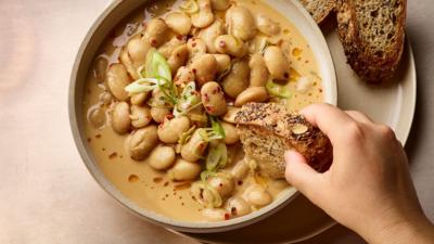 Top down view of a hand dipping bread into a bowl with butter beans in a sauce