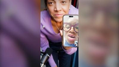 Miquita stands close to the camera, holding her phone up where you can see Andi Oliver on a video call